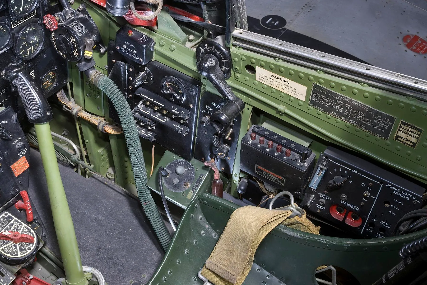 Close-up of the right side of a P-51D cockpit showing the electrical panel, engine limitations plate, homing adapter and green-painted interior structure
